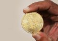 Foto asli seseorang memegang koin fisik Bitcoin sebagai ilustrasi aset kripto