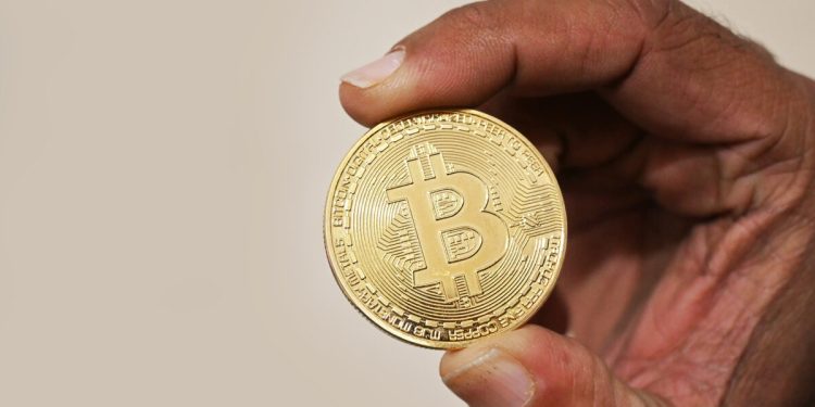 Foto asli seseorang memegang koin fisik Bitcoin sebagai ilustrasi aset kripto
