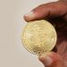 Foto asli seseorang memegang koin fisik Bitcoin sebagai ilustrasi aset kripto